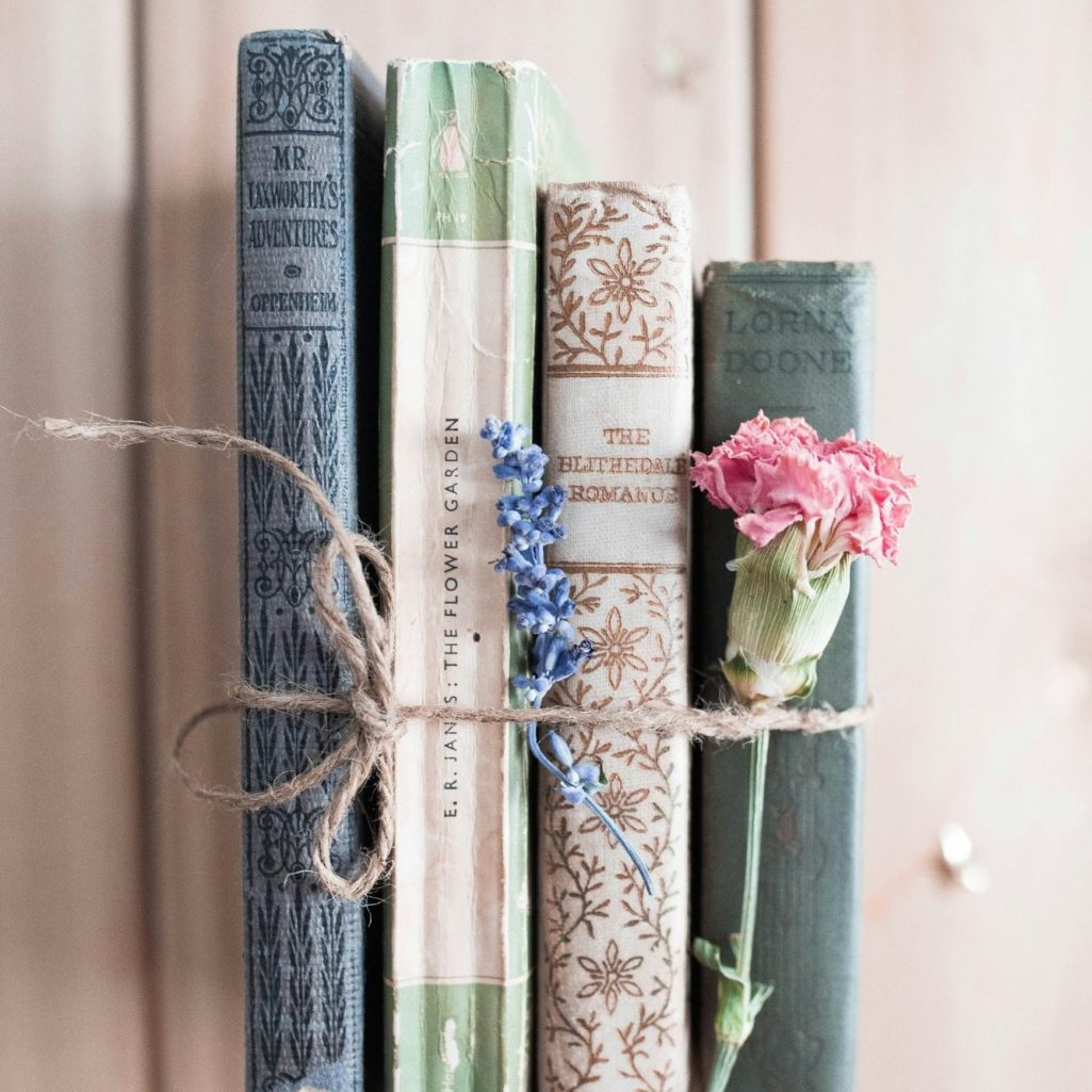 A stack of vintage books tied with twine, decorated with flowers.