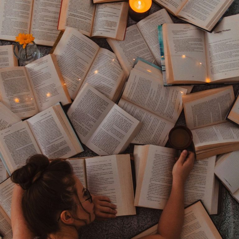 A person resting among open books and candles, creating a cozy reading atmosphere.